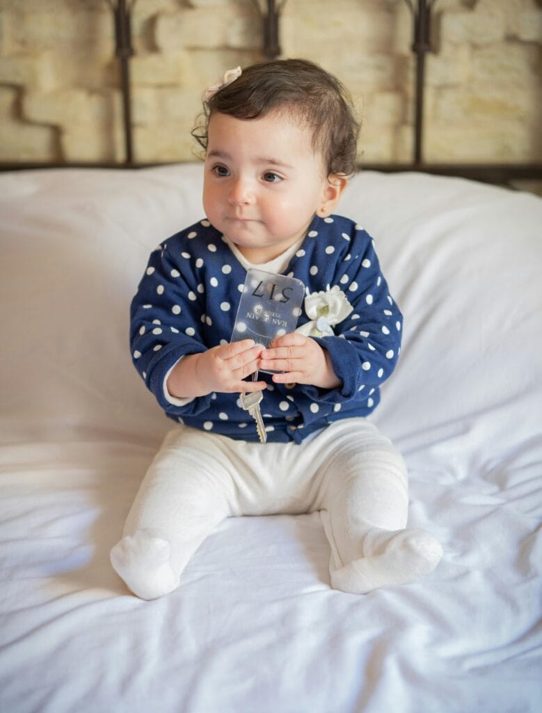 A toddler sitting on a hotel bed holding a key, highlighting family-friendly accommodations in Paris.