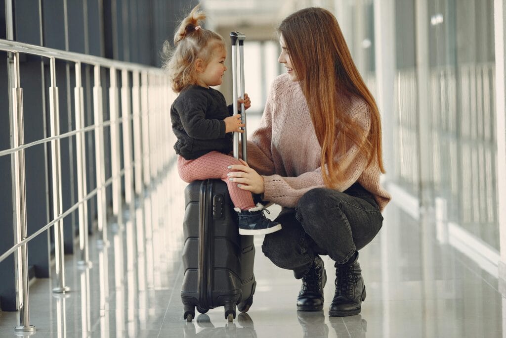 A smiling mother with her daughter and suitcase at the airport, preparing for a family trip to Paris