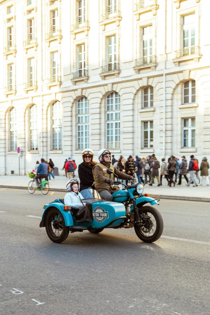 A happy family riding in a vintage sidecar motorcycle through the streets of Paris, enjoying a unique and fun way to get around the city with kids.