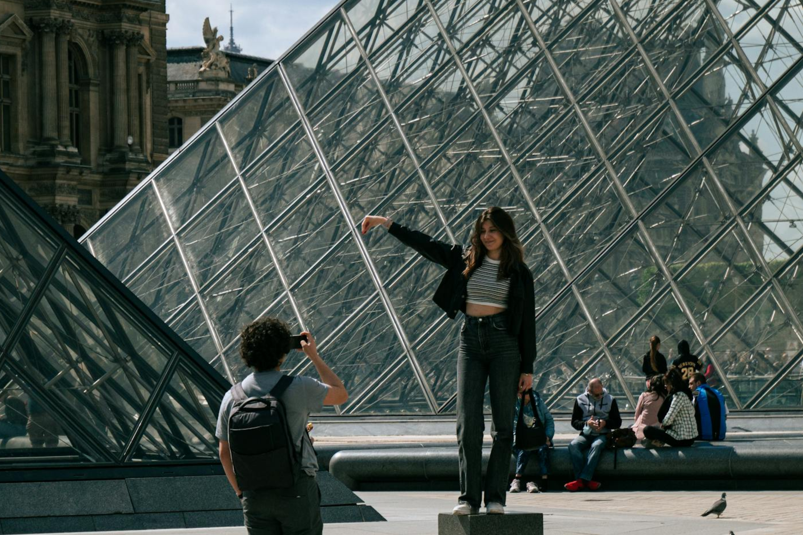 A teen girl taking a picture in front of the Louvre pyramid. One of the fun things to do in Paris with a teenager 